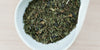 A white dish containing dry green tea and peppermint leaves.