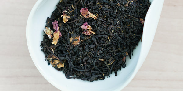 A white dish containing dry black tea leaves and rose petals