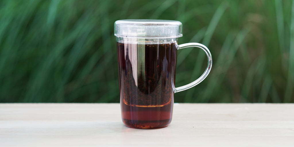 A glass cup with rose black brewing in the nested glass infuser.