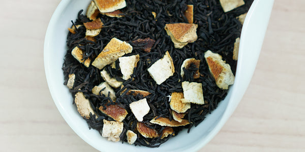 A white dish containing dry black tea leaves and orange peel