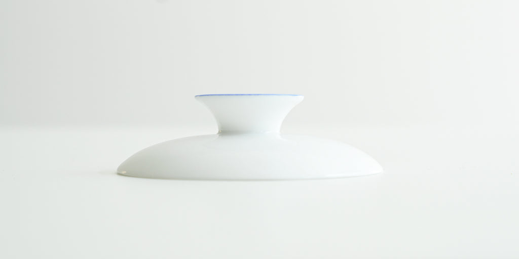 A white porcelain lid, with a blue ring around the top of the handle.