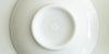 The bottom of a white dish, with Red Blossom Tea Company’s logo etched in white into the bottom of the foot.