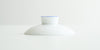 A white porcelain lid, with a blue ring around the top of the handle.