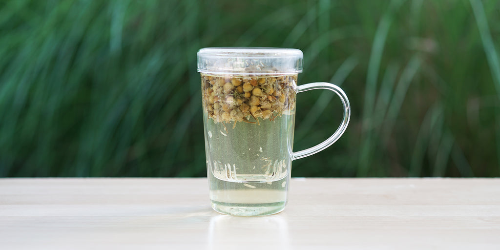 A glass cup with chamomile flowers brewing in the nested glass infuser.