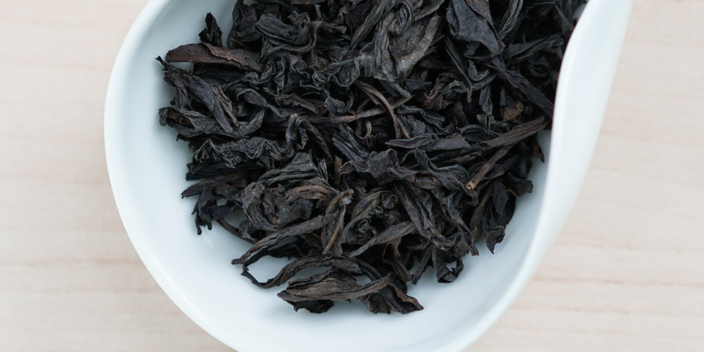 A white dish containing dry Wuyi oolong tea leaves.