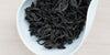 A white dish containing dry Wuyi oolong tea leaves.