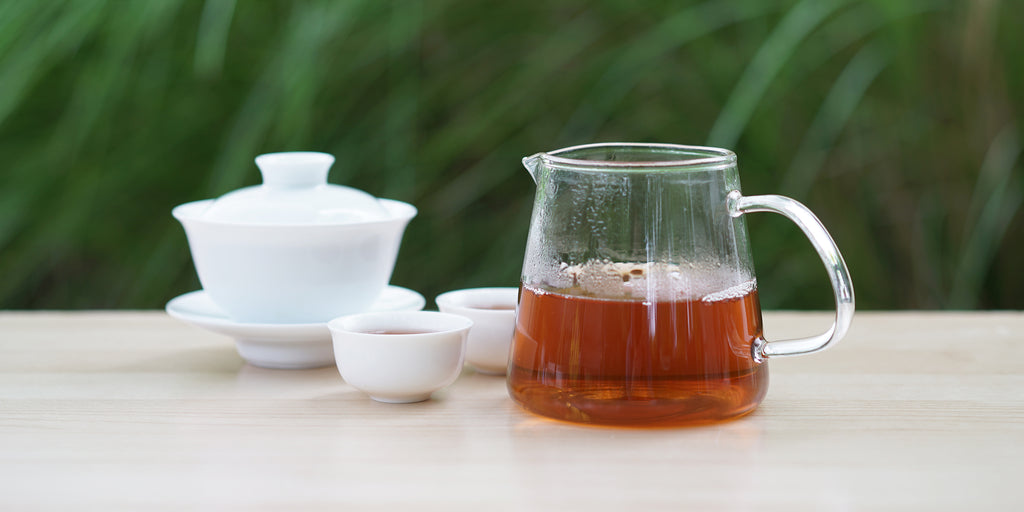 From left to right, a gaiwan, two teacups, and a glass server. The teacups and server have Wuyi oolong tea in them.
