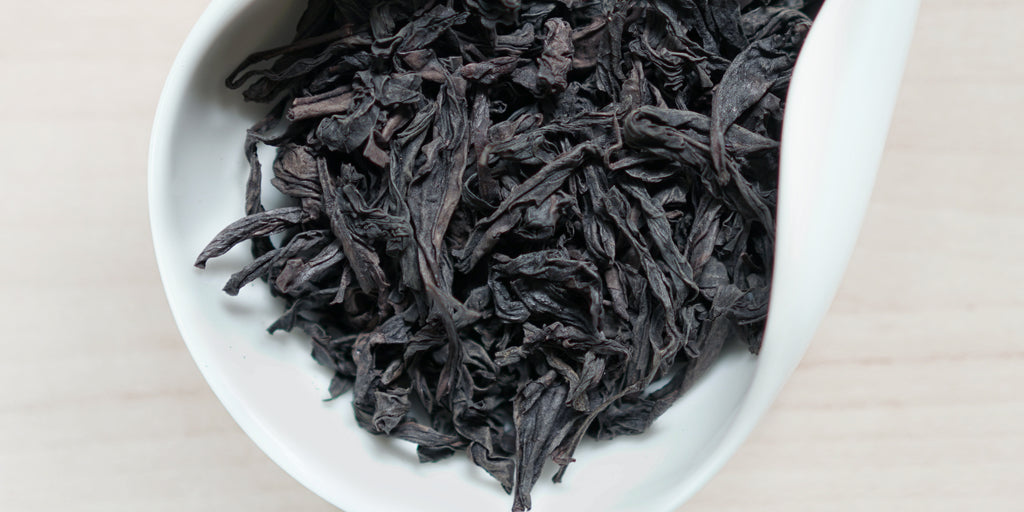 A white dish containing dry Wuyi oolong tea leaves.
