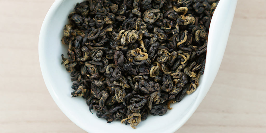 A white dish containing dry black tea leaves.